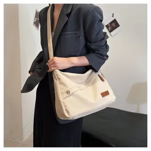 Détail du grand sac à bandoulière en toile crème avec écusson de marque marron