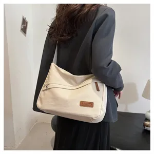 Vue de côté d'un sac bandoulière en toile crème avec étiquette en cuir sur un modèle