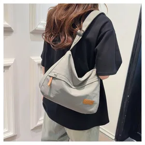 Vue détaillée d'un grand sac bandoulière gris porté par un mannequin devant un mur blanc