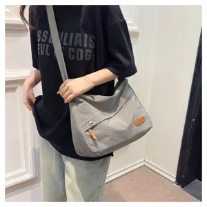 Sac bandoulière en toile grise grande capacité porté par un mannequin en mode décontracté