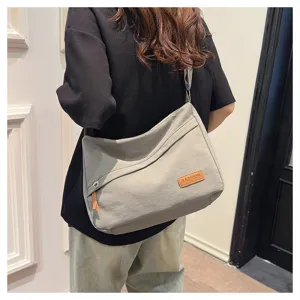 Vue détaillée d'un grand sac bandoulière en toile grise muni d'un écusson mode.