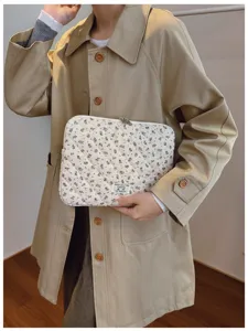 Floral quilted laptop sleeve bag with zip closure held by model in trench coat