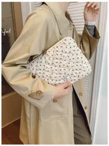 Elegant close-up of a cream quilted floral laptop sleeve bag held by a stylish model.