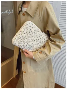 Detail of floral quilted corduroy laptop sleeve held by a person in a trench coat