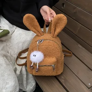 Mochila de peluche marrón con orejas de conejo y un lindo colgante de monstruo blanco.