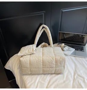 Detailweergave van de crème gewatteerde puffer-draagtas met laptop en hoofdtelefoon.