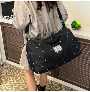 Black quilted travel duffel bag with white bows, showing detailed texture and strap.