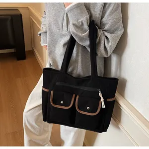 Large black corduroy tote bag with multiple pockets carried by model in casual style