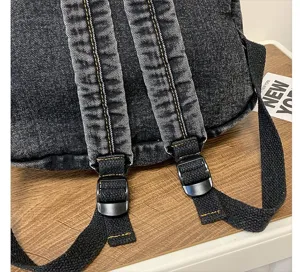 Detail view of denim backpack shoulder straps with sturdy stitching and plastic buckles