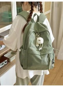 Back view of girl wearing green corduroy school backpack with fluffy monster charm