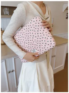 Close-up of a pink floral quilted laptop sleeve held by a woman in a lifestyle kitchen setting.