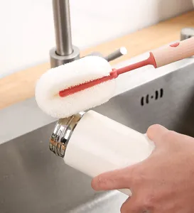 Detalle de un cepillo de esponja con mango largo limpiando una taza de cerámica blanca