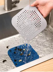 Water flowing over gray and blue silicone drain hair catchers in a modern kitchen sink.