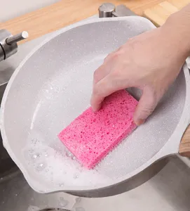 Detail of a pink wood pulp cotton sponge scrubbing a speckled pan with suds