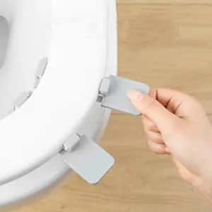 Close-up view of a hand lifting a white toilet seat lid using a grey plastic lifter handle