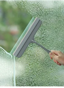 Foto de acción de un limpiacristales de goma gris limpiando gotas de agua de una ventana.