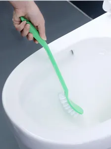 Close-up of a green plastic toilet brush with curved bristles cleaning a white toilet bowl