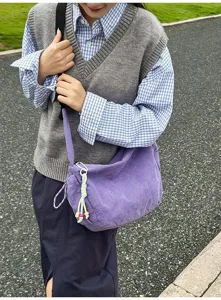 Detailansicht einer lila Cord-Umhängetasche, getragen von einem Modell in Freizeitkleidung.