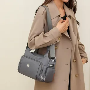 Close-up of a grey waterproof nylon crossbody bag shown worn by a model in a trench coat