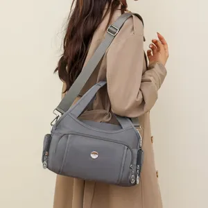 Grey nylon water-resistant shoulder bag shown worn by a model in a casual setting.