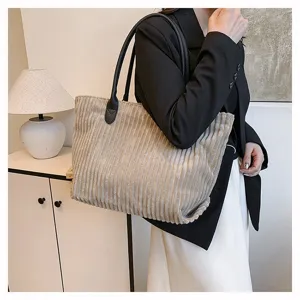 Model draagt een grote grijze corduroy draagtas in een minimalistische binnenruimte.