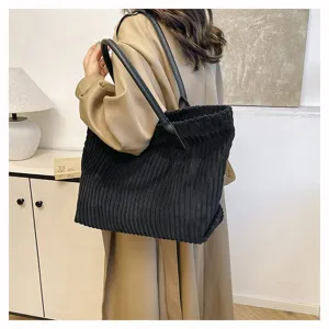 Gedetailleerd zicht op een grote zwarte corduroy tote bag, gedragen in een lifestyle setting.