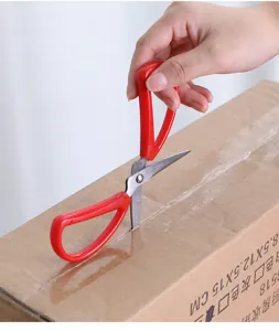 Close-up of red handled stainless steel household scissors cutting box tape efficiently