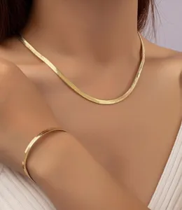Primo piano di una collana a catena di serpente piatta dorata e bracciale su modella