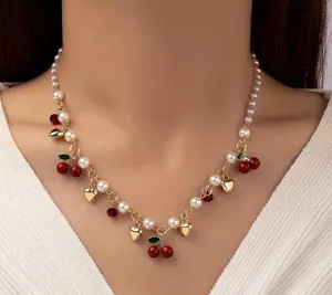 Dettaglio di una collana con ciliegie pendenti, perle finte e cuori dorati raffinati