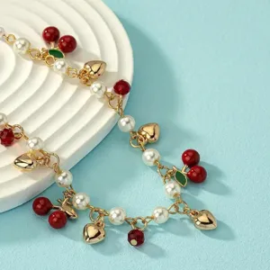 Collana con ciliegie e perle con ciondoli a cuore dorati su una catena dorata sottile.