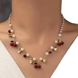 Elegante collana con ciondoli a ciliegia, perle finte e cuori dorati indossata da modella
