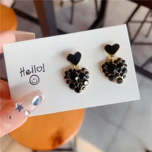 Close-up detail of heart-shaped earrings with black enamel and encrusted crystals