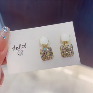 Close-up of white enamel square earrings with full rhinestone detailing.