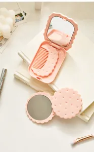 Detail view of a pink biscuit-shaped folding makeup mirror with an integrated mini comb