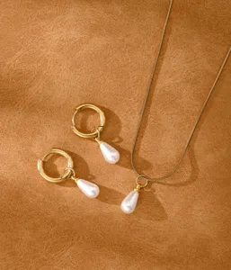 Detail of gold snake chain necklace and hoop earrings with white teardrop pearls.