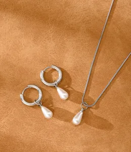 Detail view of a silver necklace and teardrop pearl earring set on a leather background