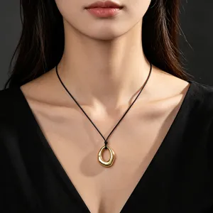 Close-up of a minimalist gold geometric pendant necklace worn on a black cord.