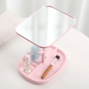 Pink desktop makeup mirror with storage base holding a brush and skincare products.