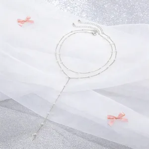 Detalle de collar plateado de doble capa con perlas sobre tela de tul blanco elegante