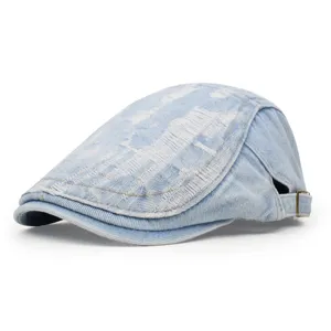 Close-up view of a light blue distressed denim flat cap on white background