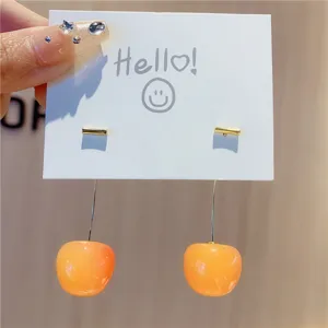 Close-up detail of glossy orange cherry drop earrings on a white Hello card.