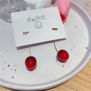 Close-up view of wine red cherry drop earrings with elegant gold curved stems on a card