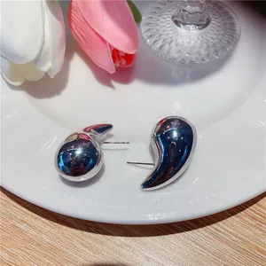 Détail rapproché de boucles d'oreilles minimalistes en forme de goutte d'eau sur assiette blanche.