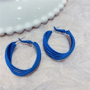 Close-up detail of matte blue multi-layer hoop earrings with textured background