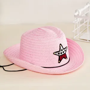Détail d'un chapeau de cowboy en paille rose pour enfants avec un écusson étoile brodé.