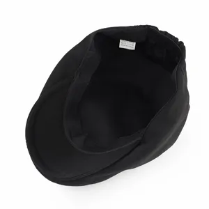 Detail view showing the black newsboy cap's interior with 100% polyester care label