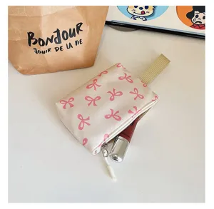 Close-up of cream cosmetic pouch with pink bow pattern and fabric strap detail
