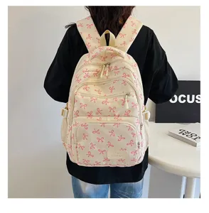 Detail view of a stylish cream backpack with pink ribbon patterns worn by a student