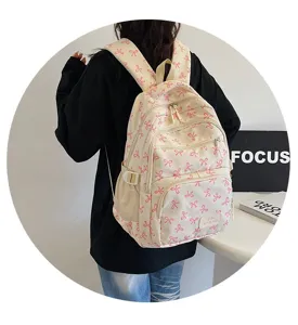 Detailed view of a cream student backpack with pink bow patterns worn by a model