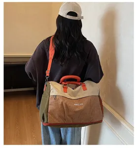 Model carrying large capacity travel duffel bag with orange handles and brown checks.